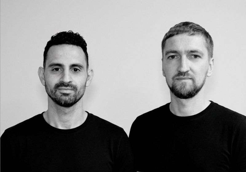 Two men in black shirts pose for professional headshot portrait against neutral gray background