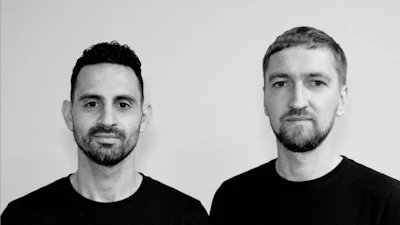 Two men in black shirts pose for professional headshot portrait against neutral gray background