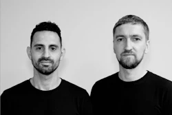Two men in black shirts pose for professional headshot portrait against neutral gray background