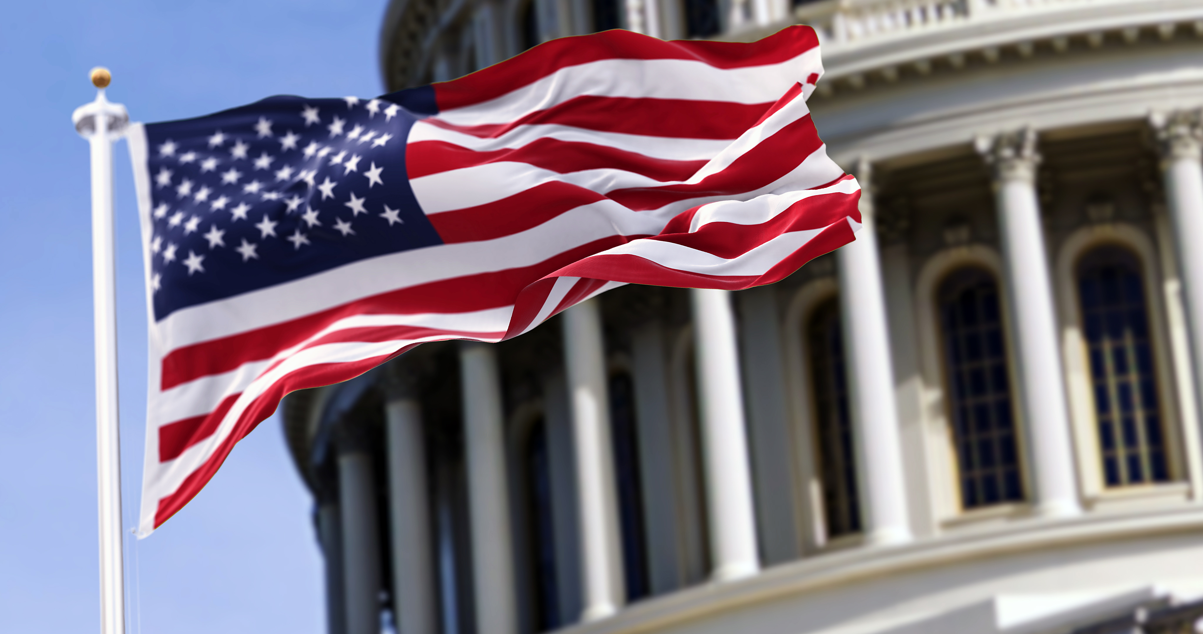American flag waving on flagpole in front of U.S. Capitol building with white columns