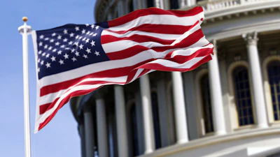 American flag waving on flagpole in front of U.S. Capitol building with white columns