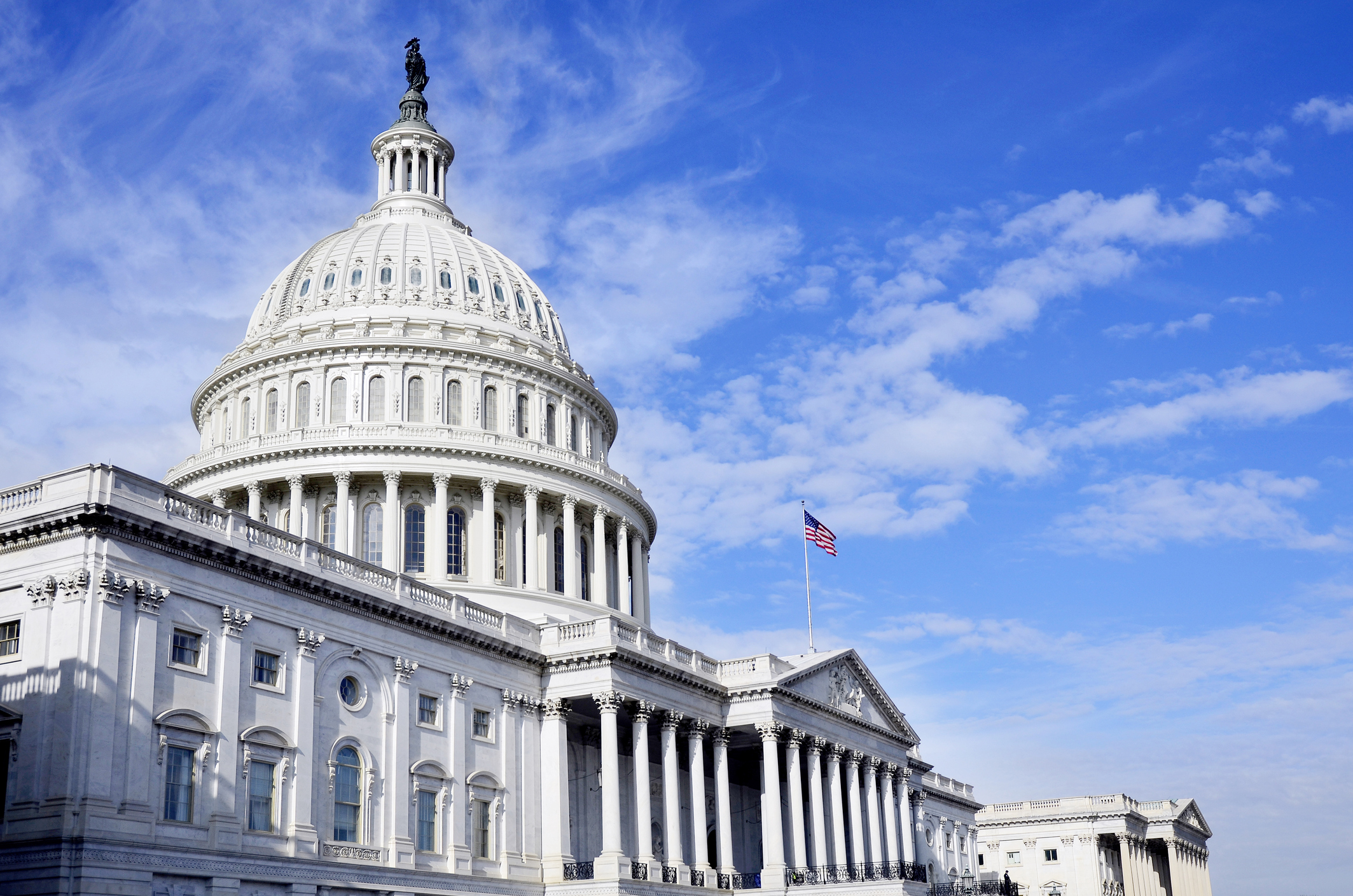 U.S. Capitol Building with white dome and neoclassical columns under blue sky with American flag