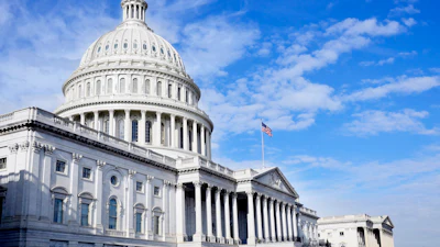 U.S. Capitol Building with white dome and neoclassical columns under blue sky with American flag