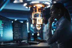 Woman in lab coat analyzing data on computer screens in modern tech facility with equipment