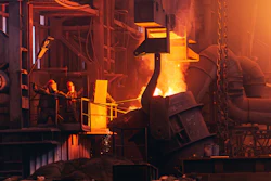 Industrial steel mill with molten metal pouring from large furnace equipment, workers on platform, intense orange glow from heat