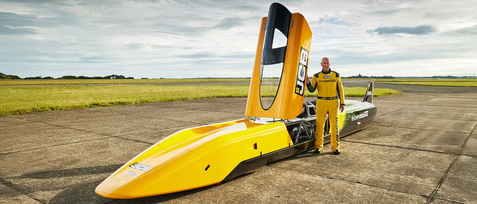 Yellow dragster with driver in racing suit on airfield runway