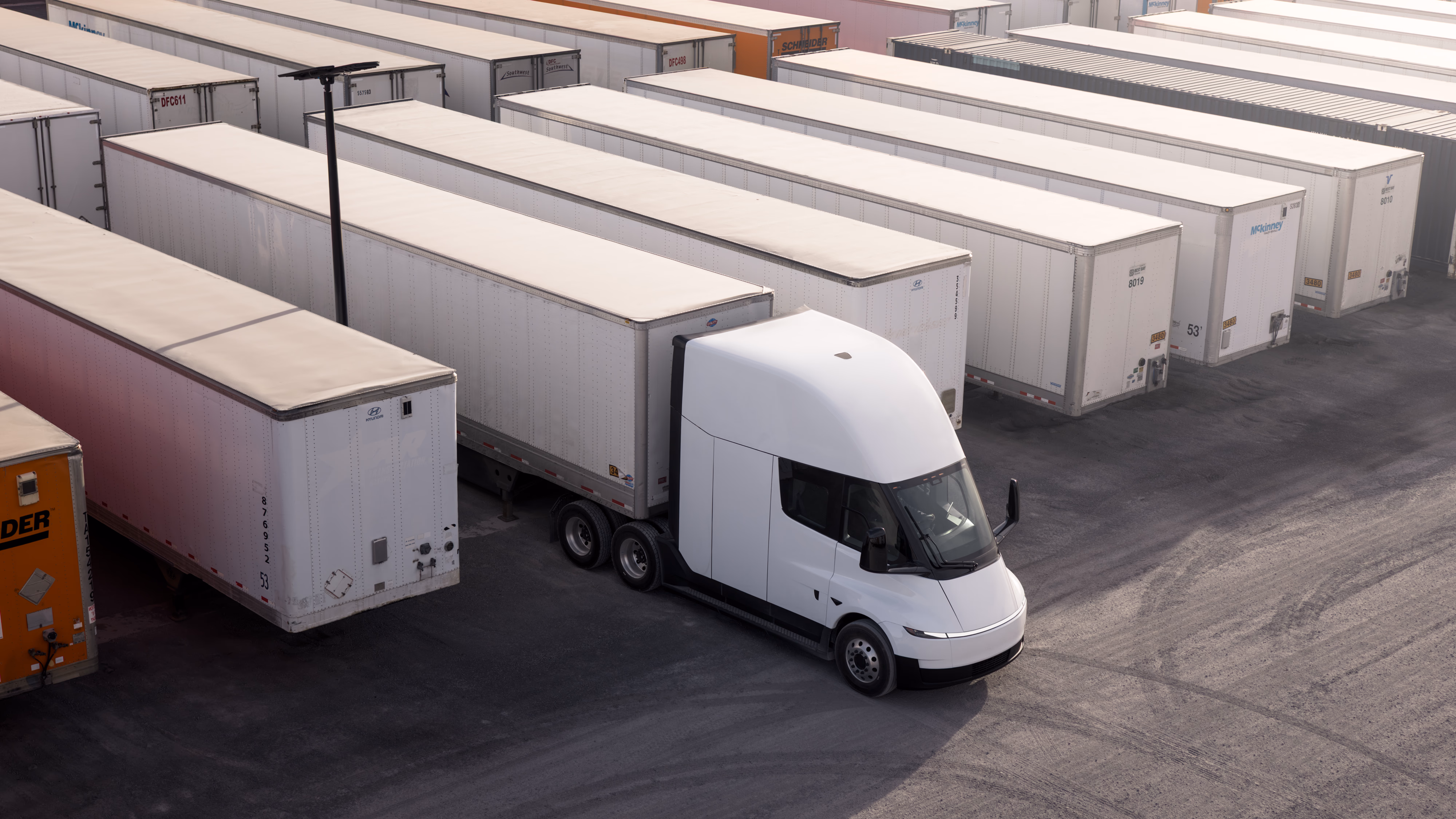 White electric truck parked among white cargo trailers in a logistics yard