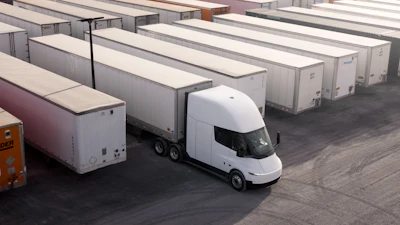White electric truck parked among white cargo trailers in a logistics yard