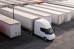 White electric truck parked among white cargo trailers in a logistics yard