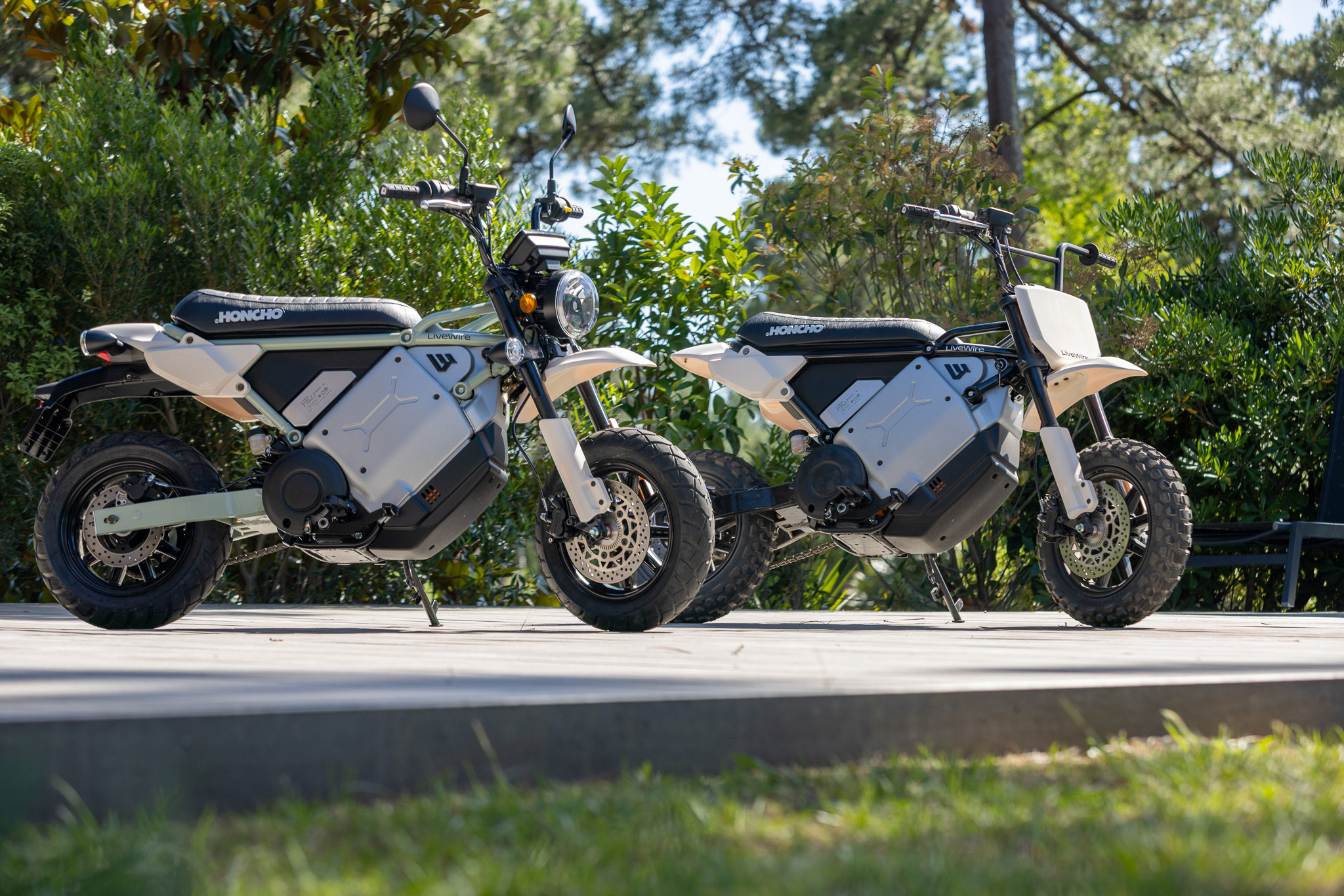 Two white and black Horwin electric scooters parked side-by-side outdoors with trees in background