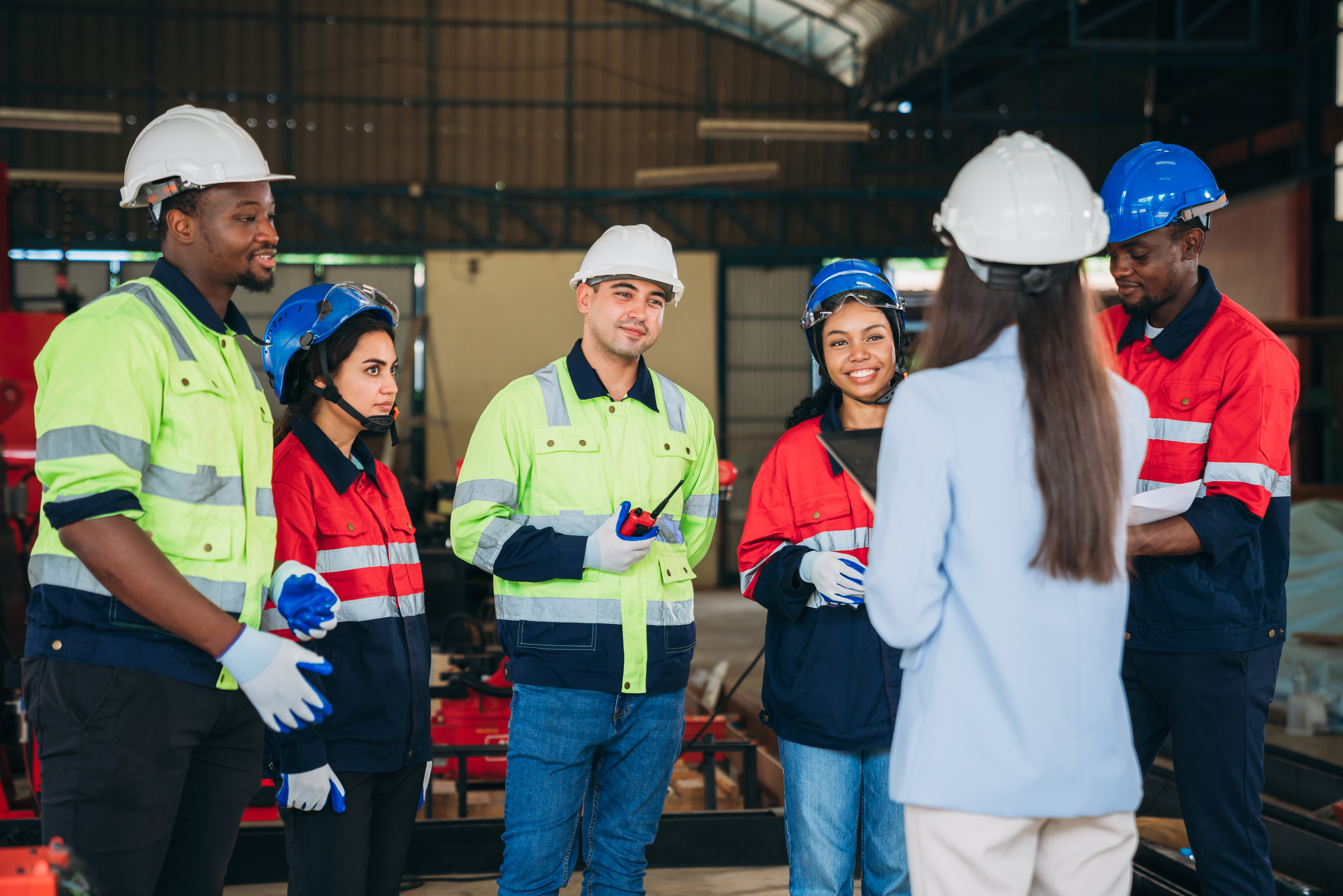 Diverse construction team in safety gear discussing project in industrial warehouse setting