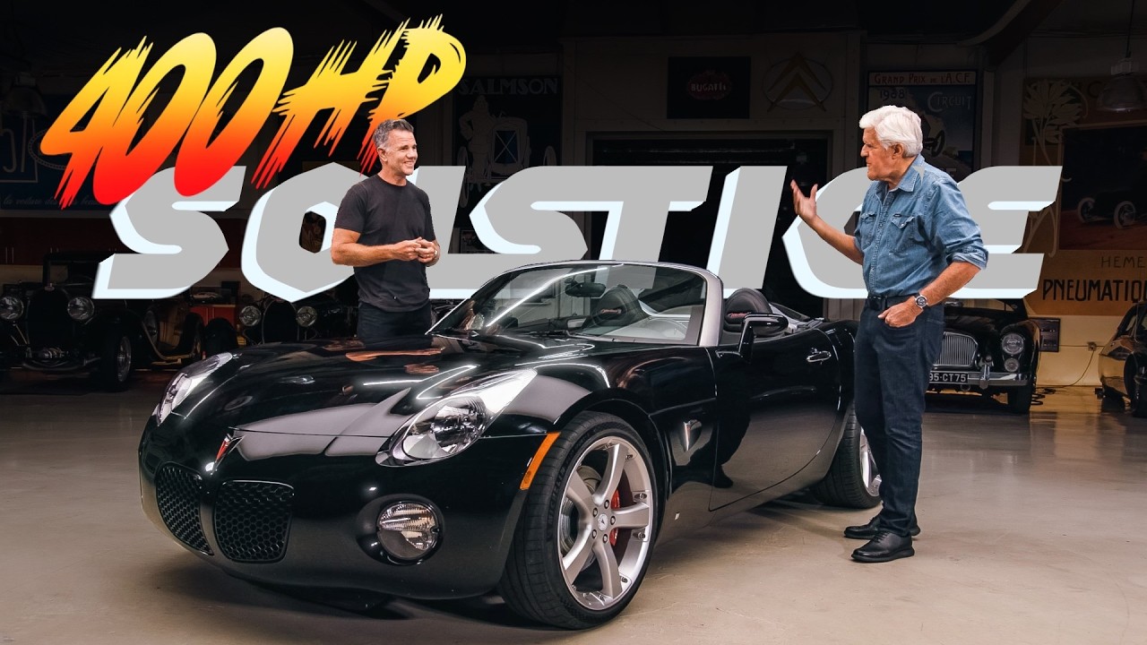 Two men discuss a black convertible sports car in a garage workshop with 400HP Solitaire branding visible
