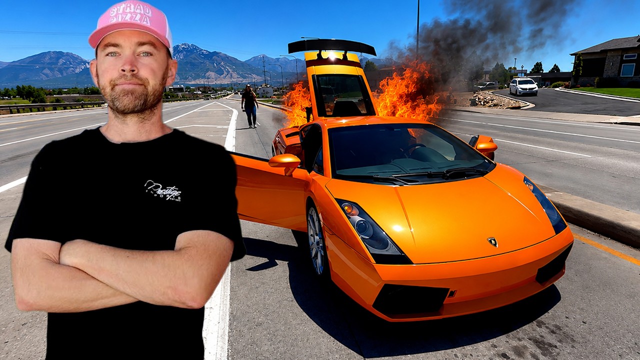 Man in pink cap posing beside burning orange Lamborghini on highway with mountains in background