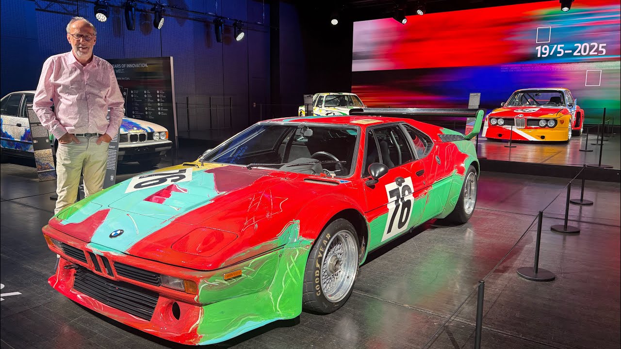 Vintage BMW race car with colorful red, green, and cyan livery displayed at automotive exhibition with spectator
