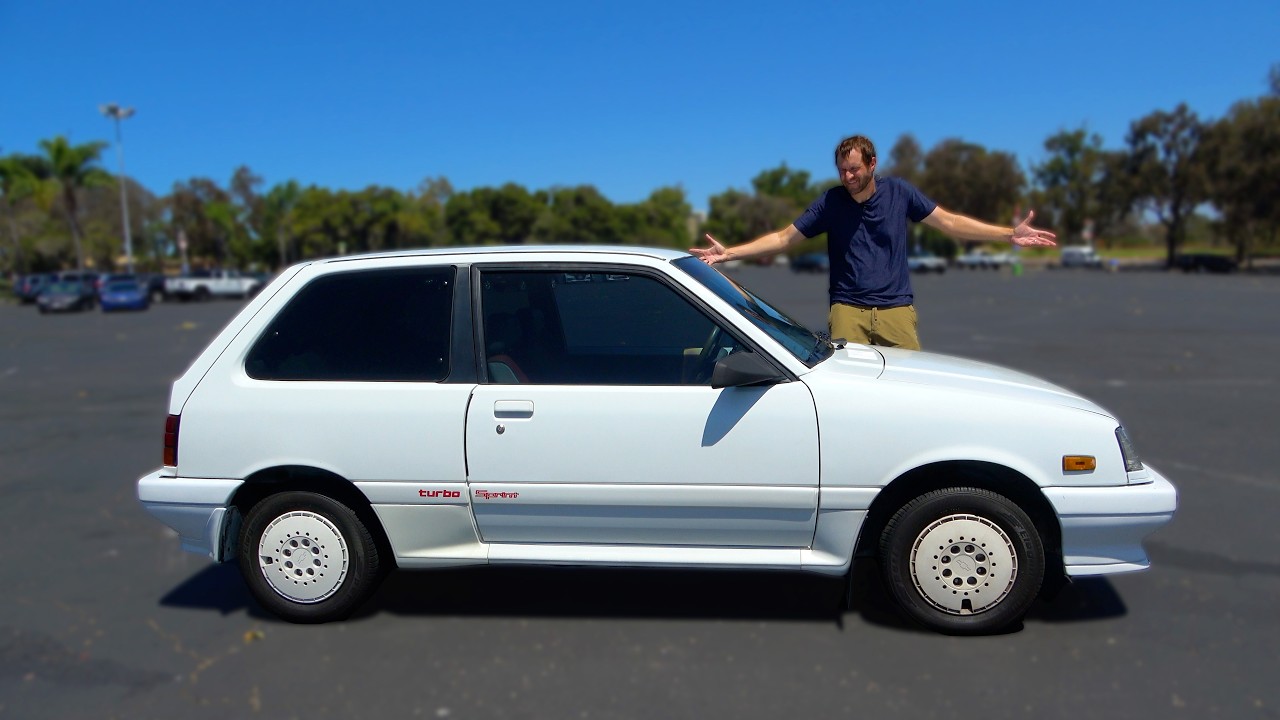 Man posing on white 1980s hatchback car in sunny parking lot with trees in background