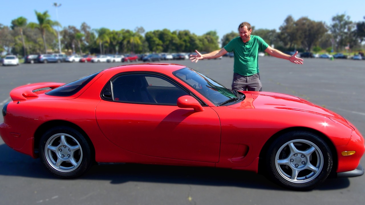 Man in green shirt posing on red sports car in parking lot with trees in background