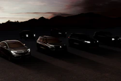 Multiple luxury vehicles parked at dusk with illuminated headlights against a mountain backdrop at sunset