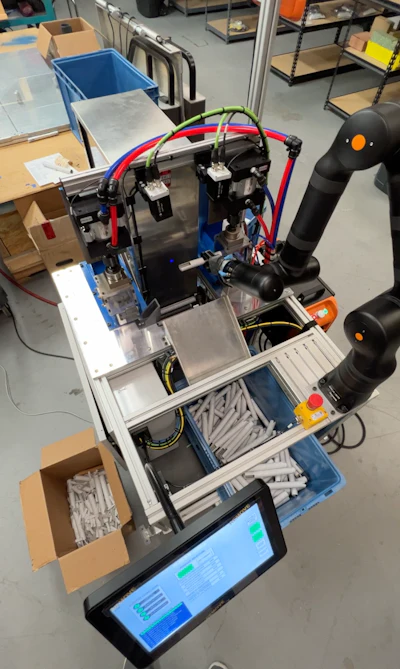 3D printer with blue frame, red and green filament tubes, and black extruder mounted on metal base with control screen in workshop setting