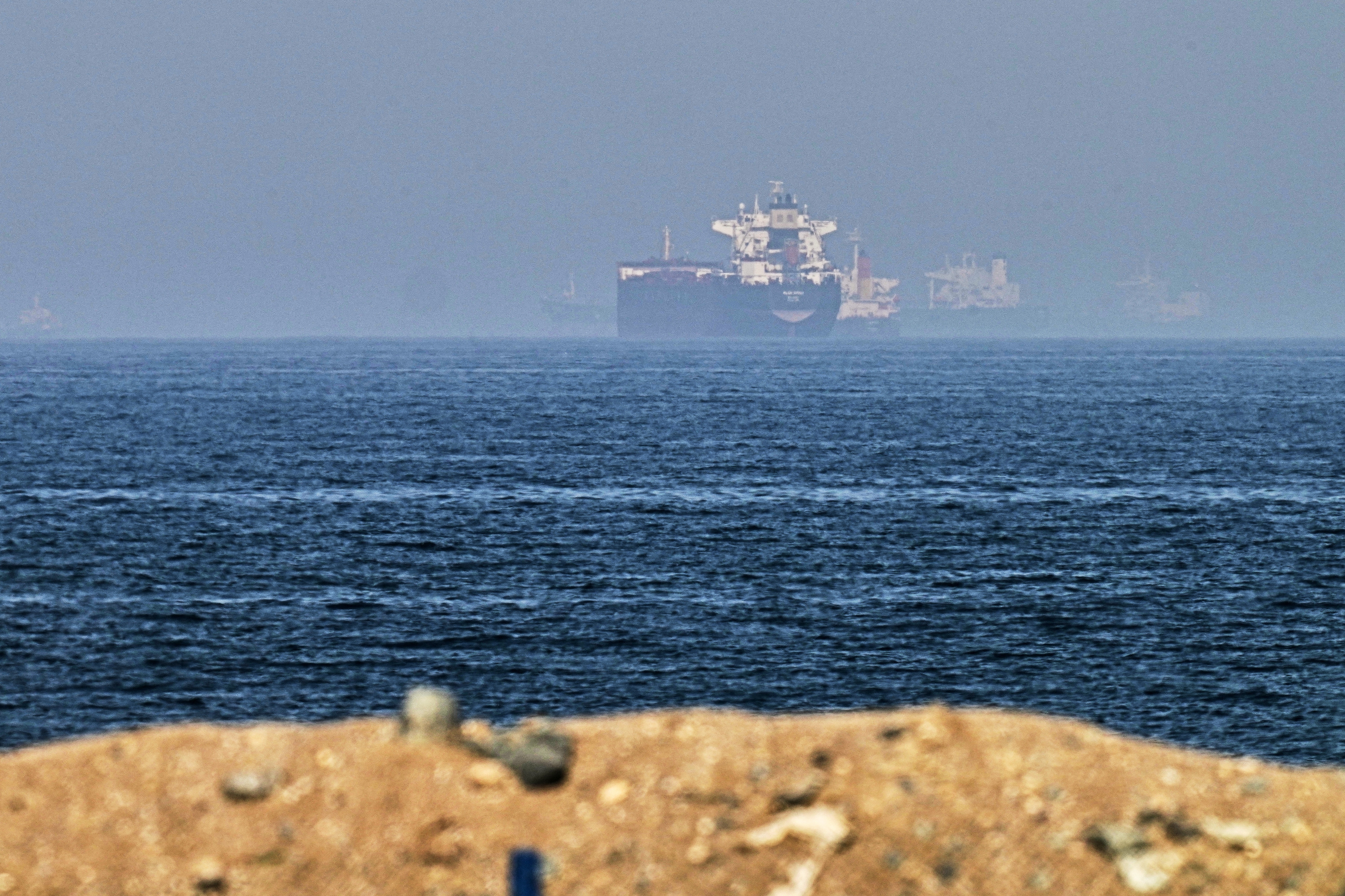 Large cargo ship on the ocean horizon viewed from a sandy beach under clear sky