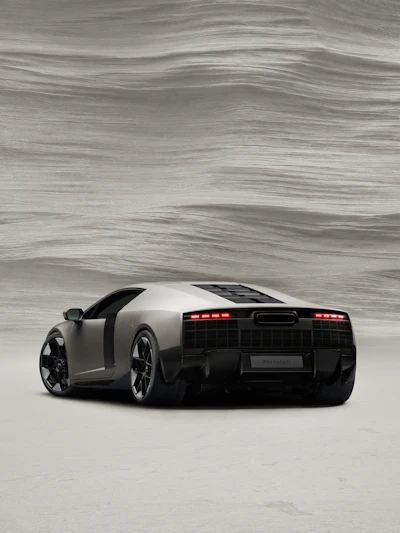 White and black Lamborghini sports car with red taillights, rear three-quarter view against textured gray background
