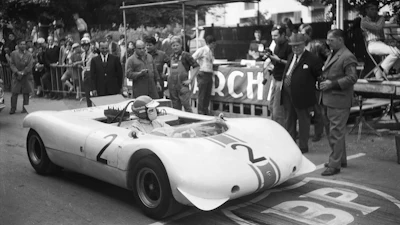 Vintage white racing car number 2 displayed at outdoor event with spectators and officials in 1950s setting