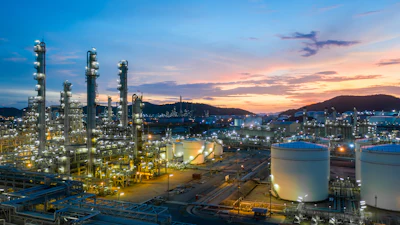 Industrial petrochemical refinery complex illuminated at sunset with tall distillation towers and storage tanks against twilight sky