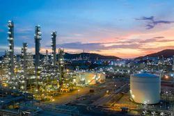 Industrial petrochemical refinery complex illuminated at sunset with tall distillation towers and storage tanks against twilight sky