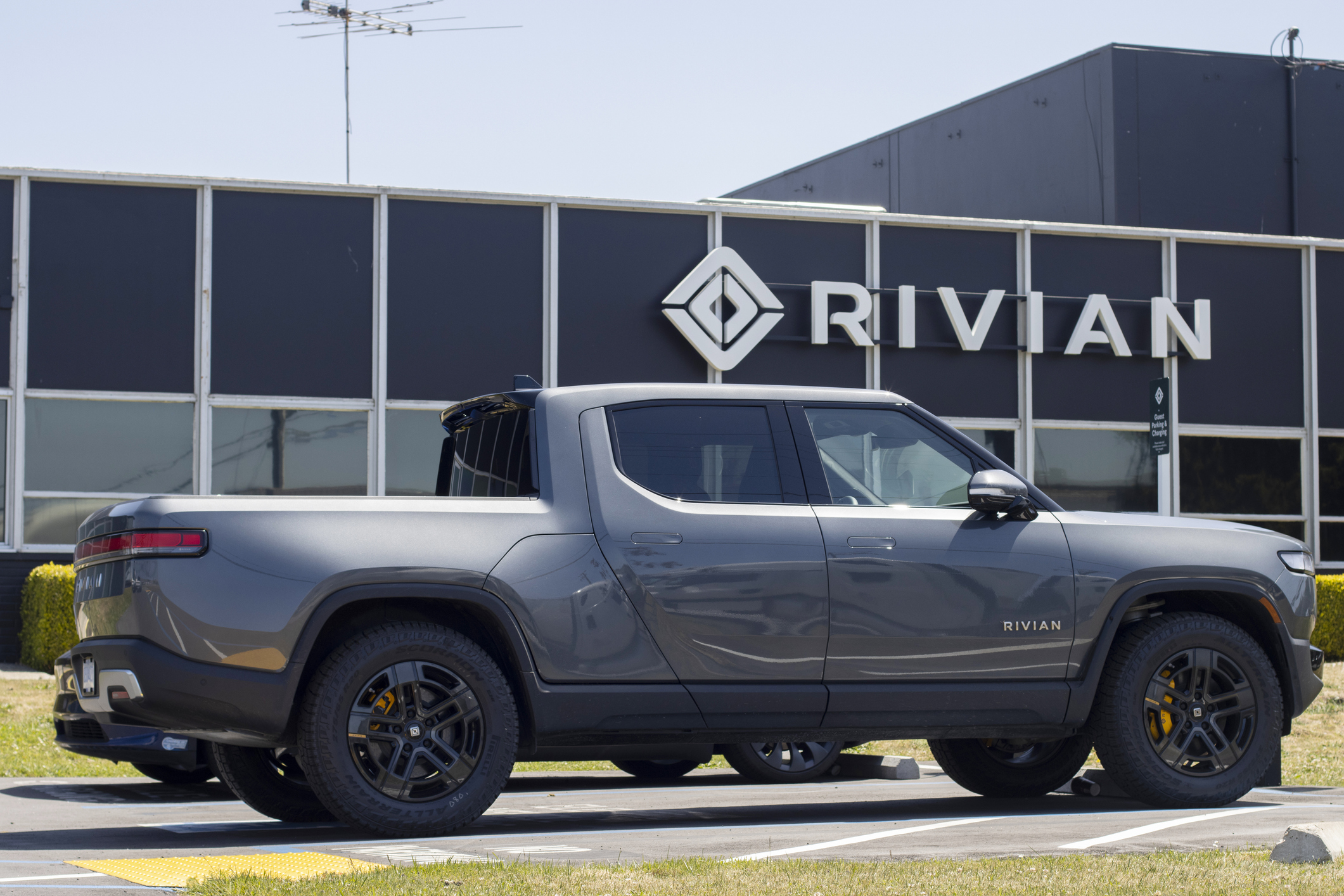Rivian R1T electric truck parked in front of Rivian corporate building with logo signage