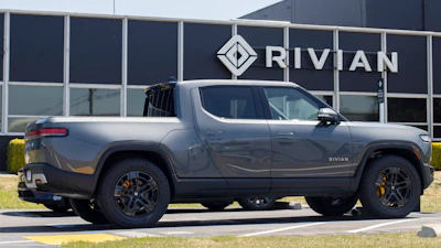 Rivian R1T electric truck parked in front of Rivian corporate building with logo signage