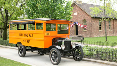 Vintage 1927 Ford Model T truck labeled 'Blue Bird No. 1' parked in front of a brick schoolhouse with bell tower