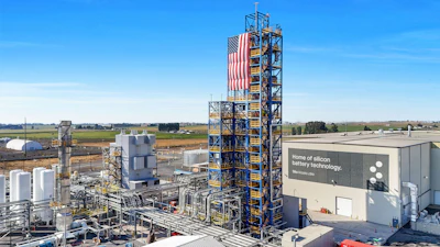 Industrial silicon battery technology manufacturing facility with tall tower and American flag in rural landscape