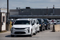 Row of white and dark vehicles parked in industrial lot with factory building in background