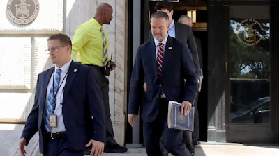 Government officials exiting federal building with official seal visible on entrance wall