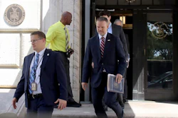 Government officials exiting federal building with official seal visible on entrance wall
