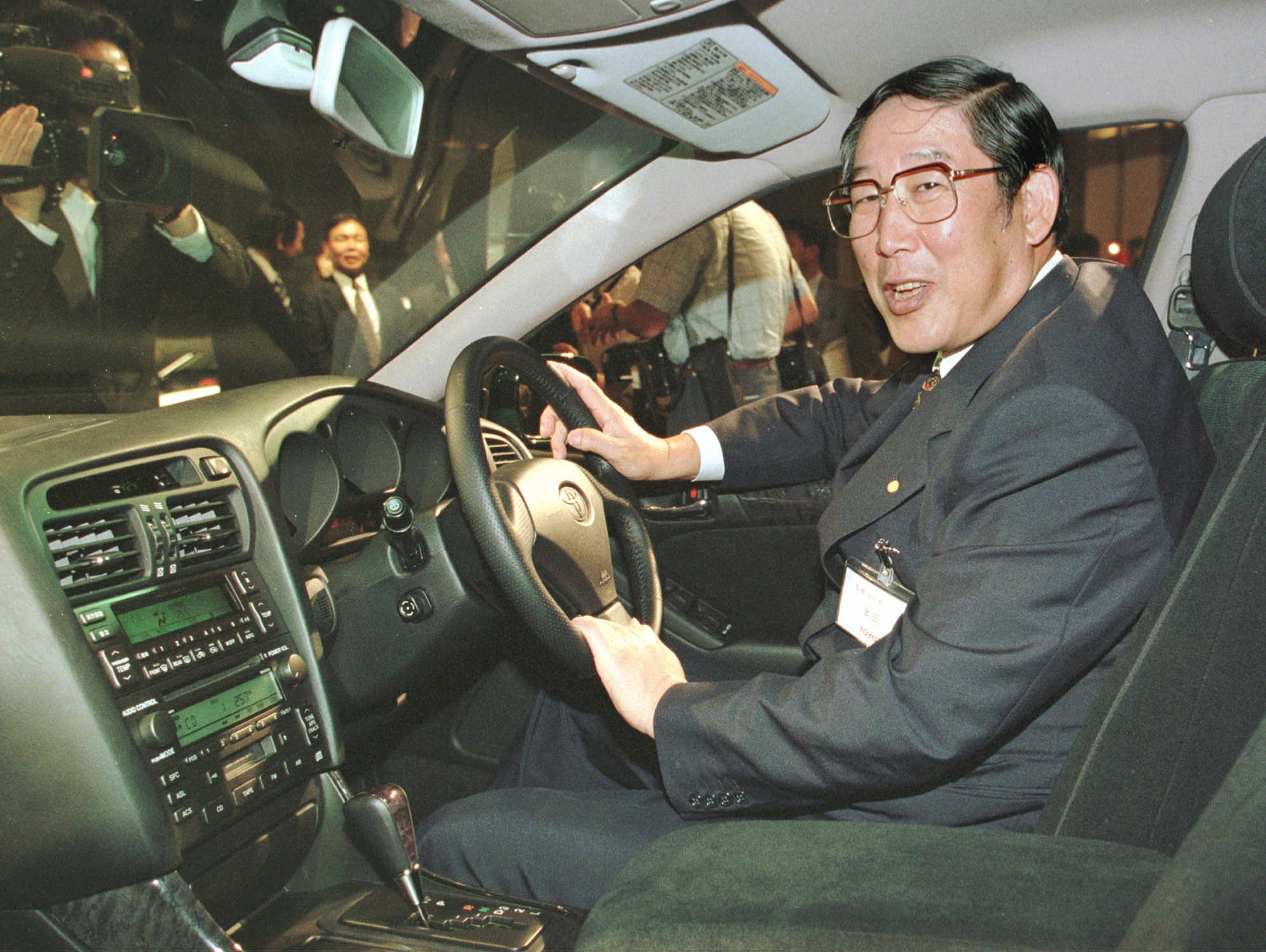 Man in glasses and suit demonstrating car interior at public automotive event