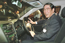 Man in glasses and suit demonstrating car interior at public automotive event