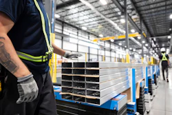Industrial warehouse worker in safety gear inspecting stacked metal rectangular tubes on blue pallets