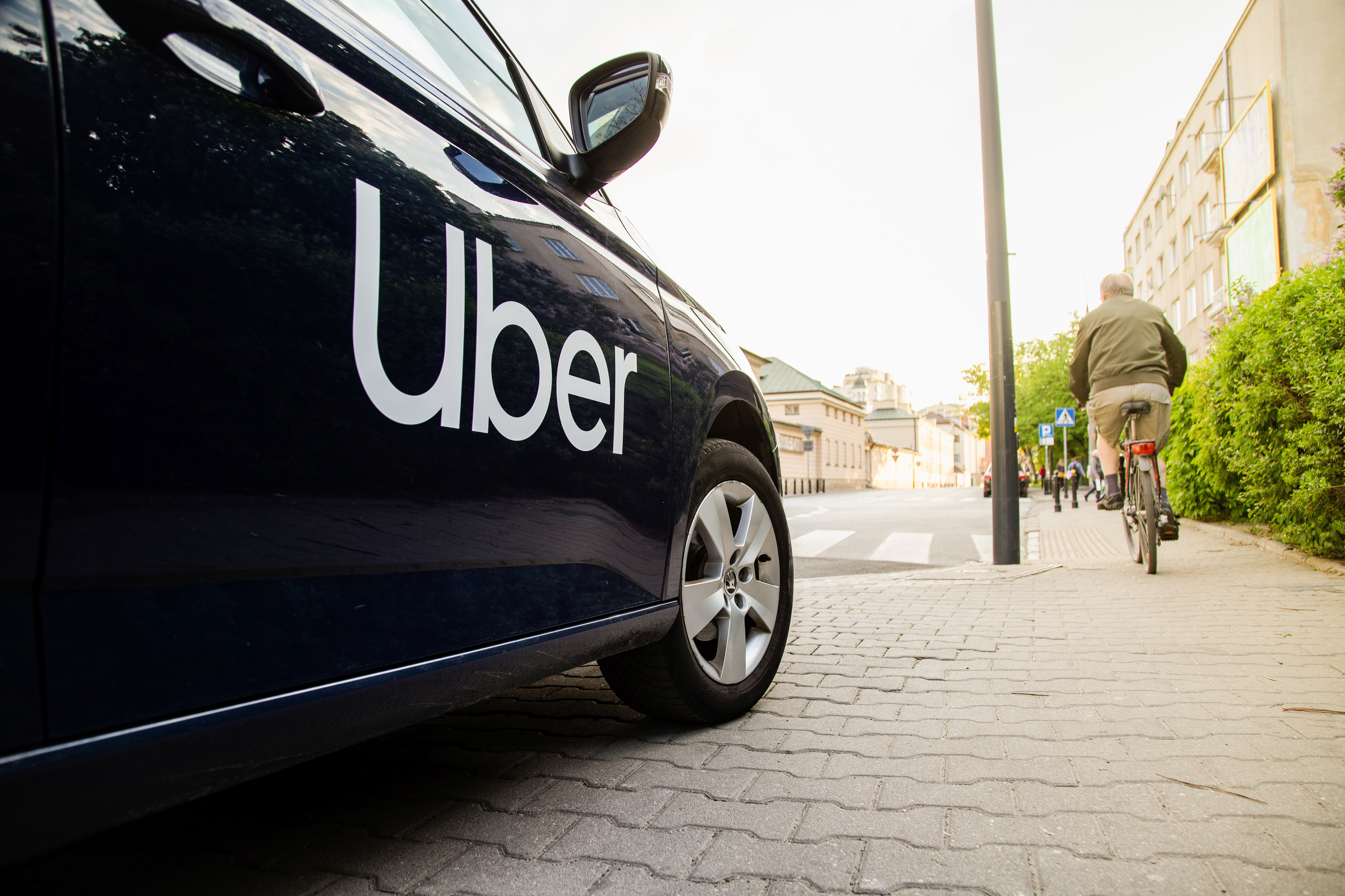 Uber branded black vehicle parked on urban street with cyclist and buildings in background