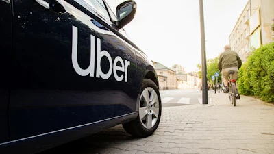 Uber branded black vehicle parked on urban street with cyclist and buildings in background