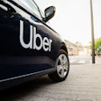 Uber branded black vehicle parked on urban street with cyclist and buildings in background