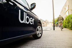 Uber branded black vehicle parked on urban street with cyclist and buildings in background