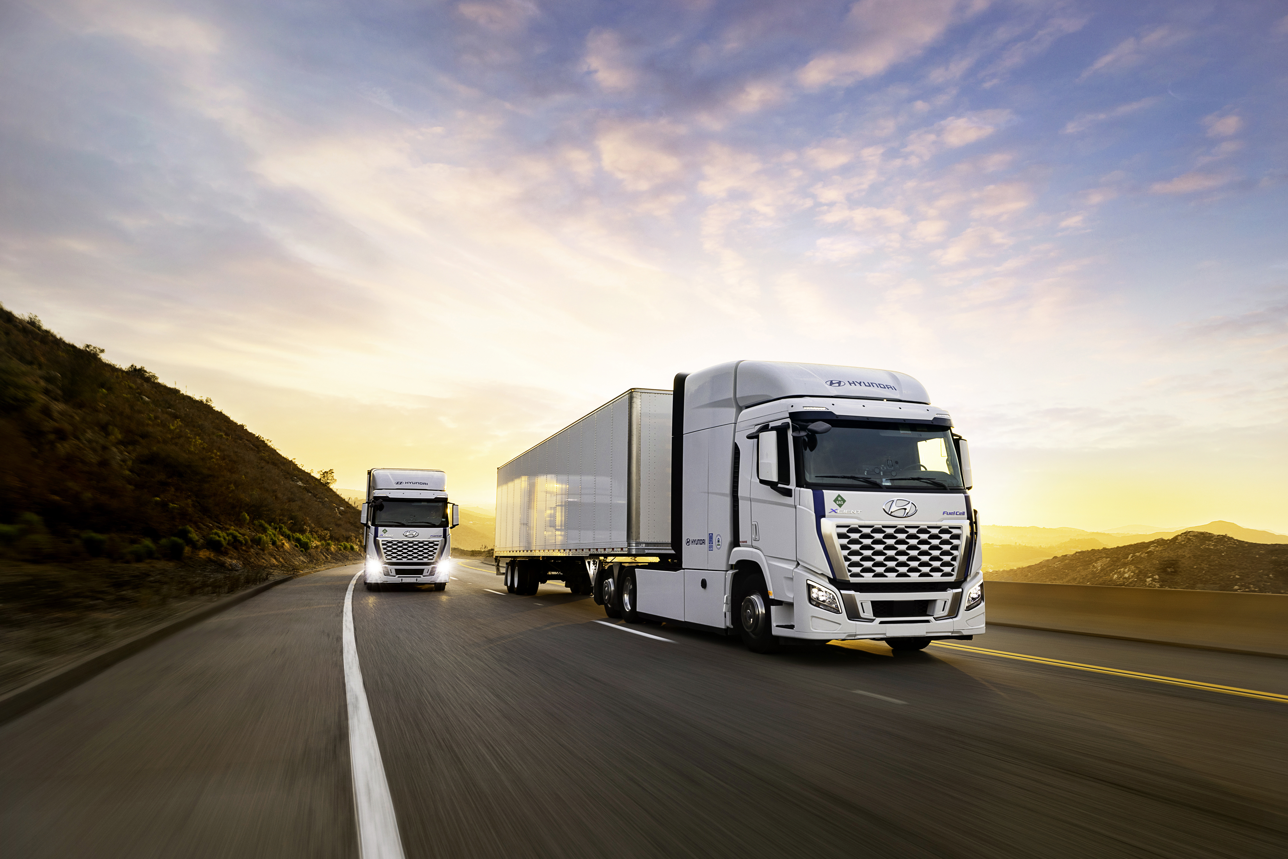 Two white Hyundai trucks driving on a highway during golden hour with mountains in background