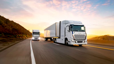 Two white Hyundai trucks driving on a highway during golden hour with mountains in background