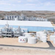 Industrial processing plant with large storage tanks, manufacturing buildings, and equipment in arid landscape