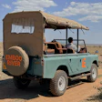 Turquoise safari vehicle with canvas canopy and 'Emboo River' branding parked in African savanna landscape