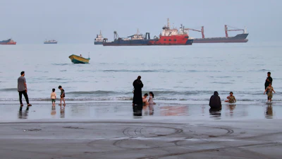 People spend time at a beach as commercial vessels are anchored in the Strait of Hormuz off Bandar Abbas, Iran, Aug. 5, 2026.