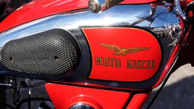Vintage red Moto Guzzi motorcycle with winged logo on fuel tank and black mesh side panel