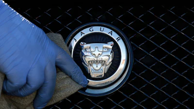 Jaguar logo emblem on vehicle grille with gloved hand touching chrome badge