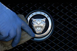 Jaguar logo emblem on vehicle grille with gloved hand touching chrome badge