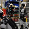 Humanoid robots in an industrial laboratory with equipment, shelving, and blue machinery in background